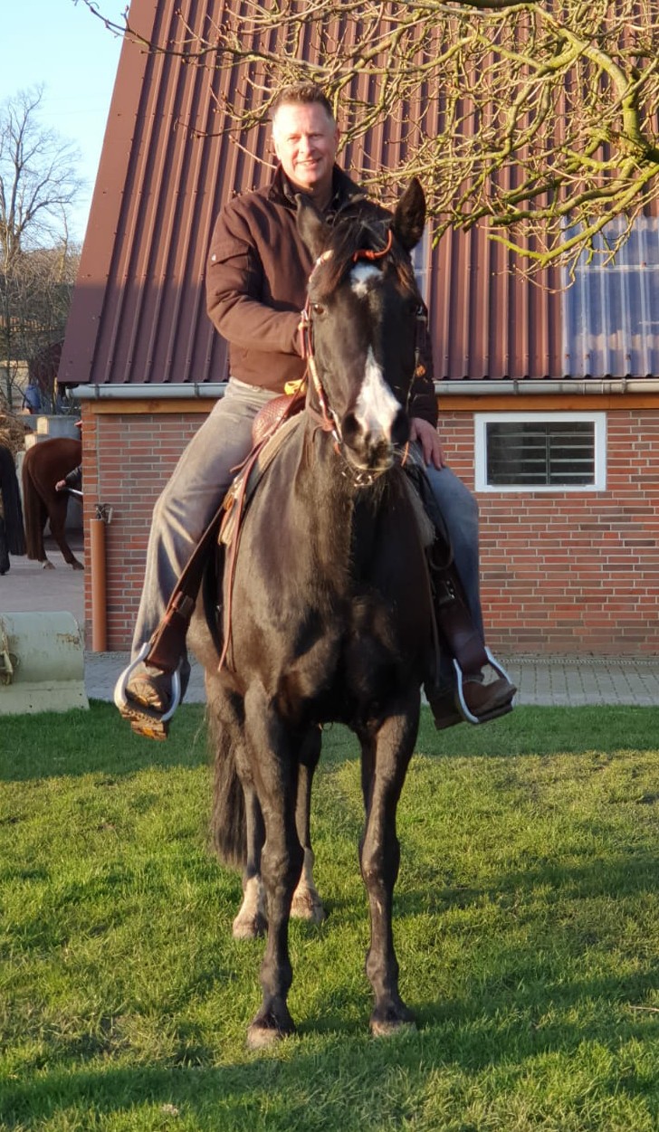 Rhetoriktrainer Ike Fast auf einem schwarzen Pferd vor einem Stall.