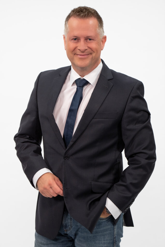 Entspannter Kommunikationstrainer Ike Fast, eine Hand in Hosentasche, im Anzug mit lässiger Jeans