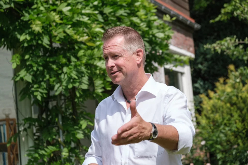 Ein Bild von Rhetoriktrainer Ike Fast mit Grünpflanzen im Hintergrund.