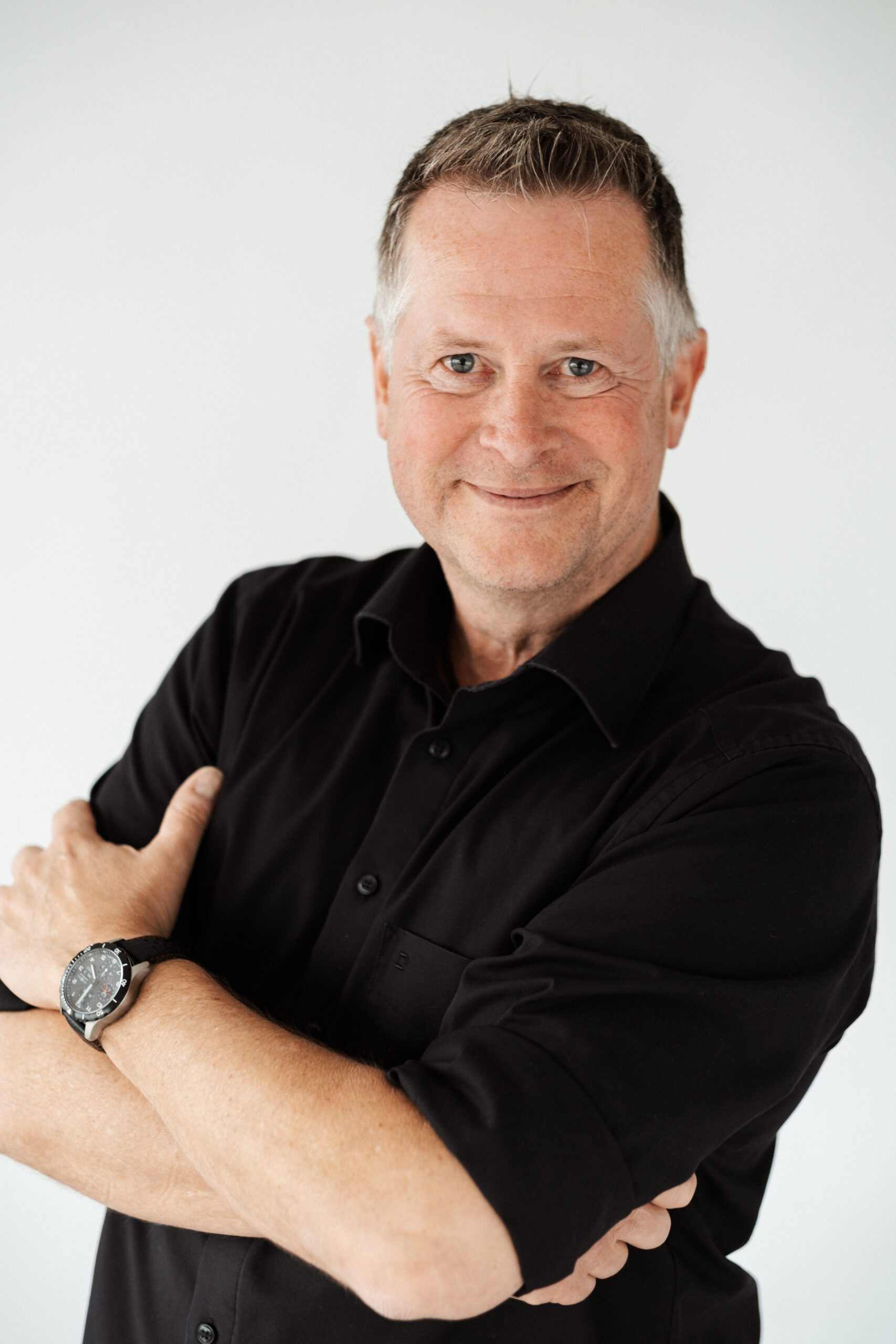 Rhetoriktrainer Ike Fast steht lächelnd mit verschränkten Armen vor einer hellgrauen Wand.