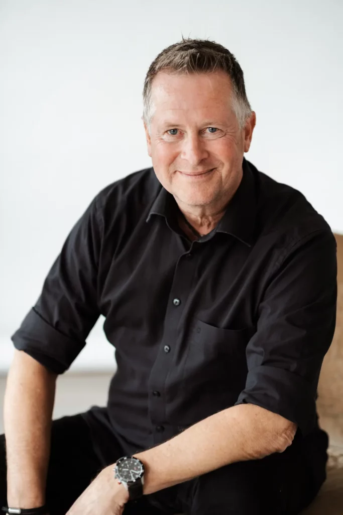 Rhetoriktrainer Ike Fast sitzt lächelnd auf einem Stuhl, der Blick ist der Kamera zugewandt.