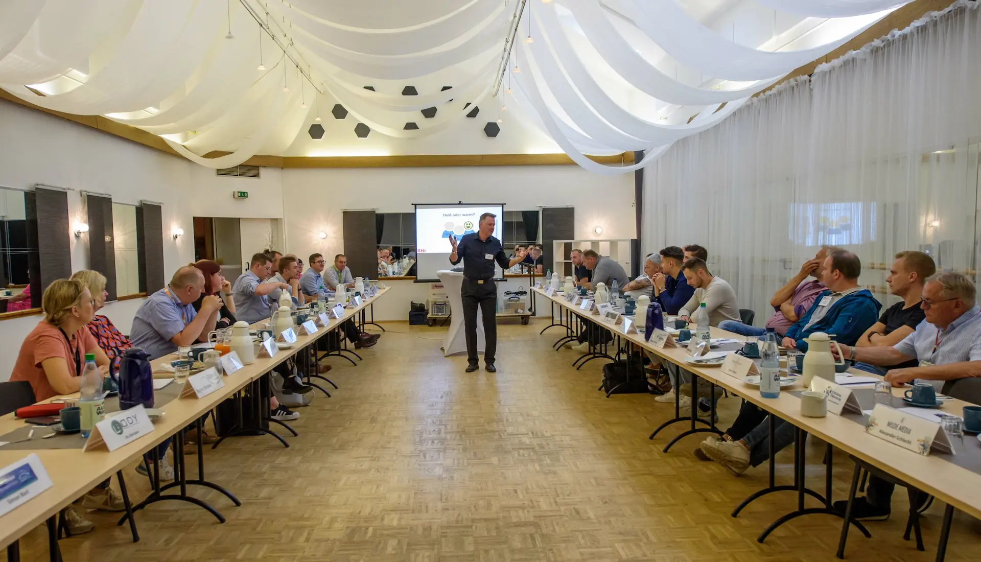 Rhetoriktrainer Ike Fast hält Präsentation vor interessierten Leuten, Projektor im Hintergrund.