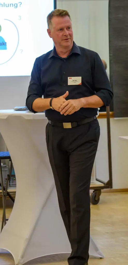 Selbstbewusster Rhetoriktrainer Ike Fast präsentiert Coaching für Führungskräfte, Hände zusammengeschlagen, im Raum laufend.