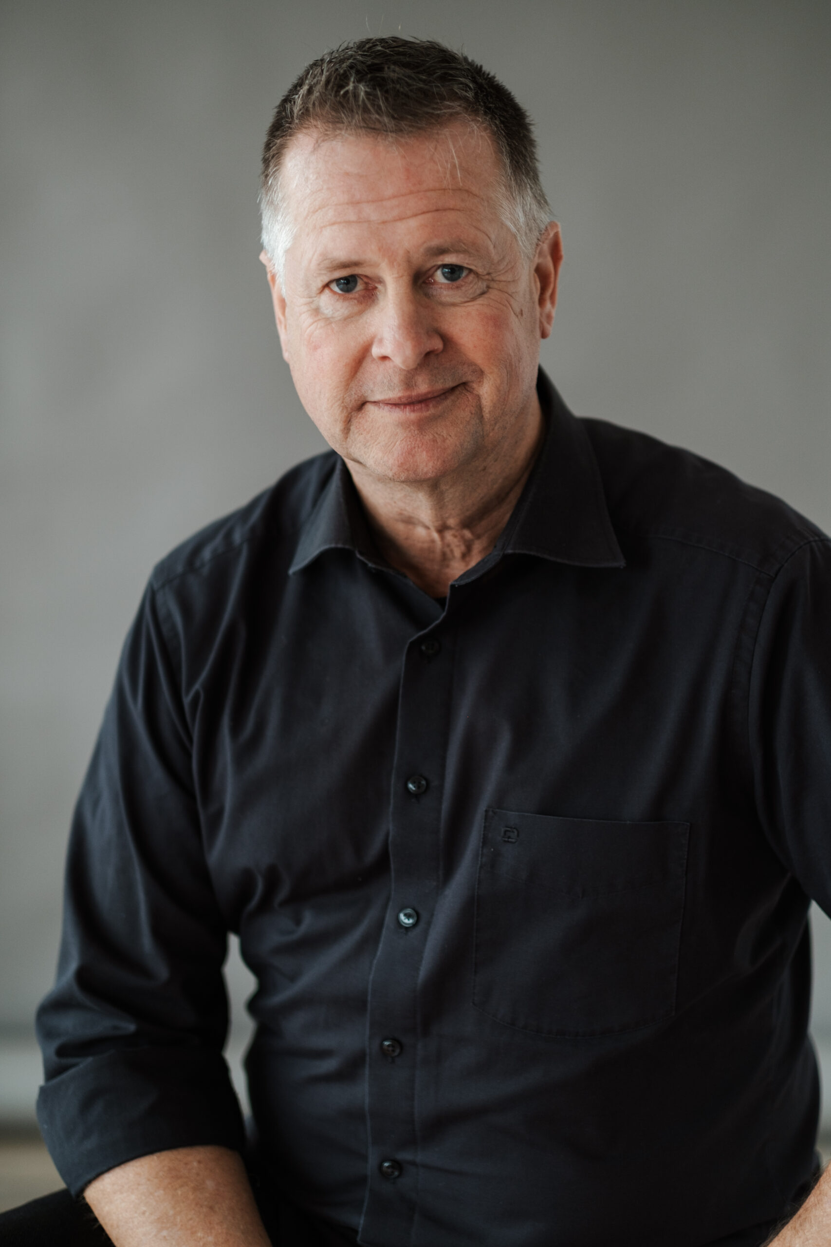 Ein Bild von Rhetoriktrainer Ike Fast im schwarzen Hemd vor einem grauen Hintergrund.